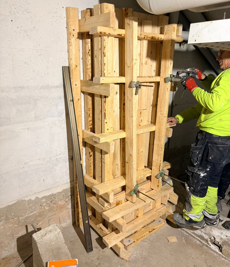 A construction worker securing a wooden concrete column formwork with clamps in a basement.