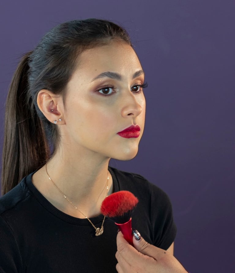 Maquilladora profesional aplicando rubor a una modelo con lápiz labial rojo y una cola de caballo