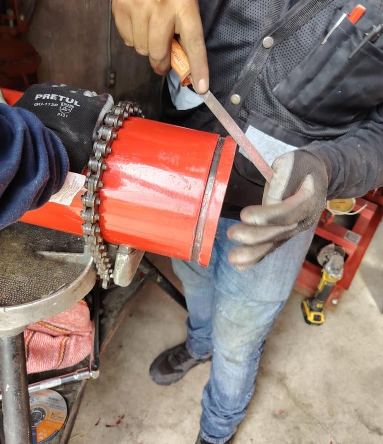 A plumber uses a metal file to smooth the edge of a red PVC pipe secured by a chain vise tool.