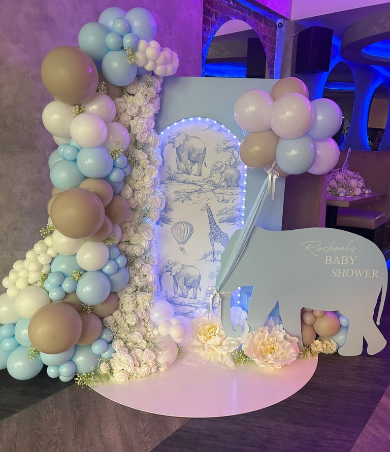 A baby shower decoration features a blue elephant cutout with 'Rachael's Baby Shower' text, surrounded by white, blue, and