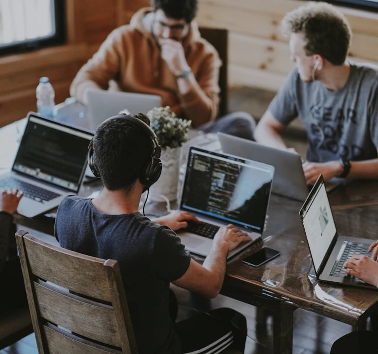 a group of people sitting around a table with laptops
