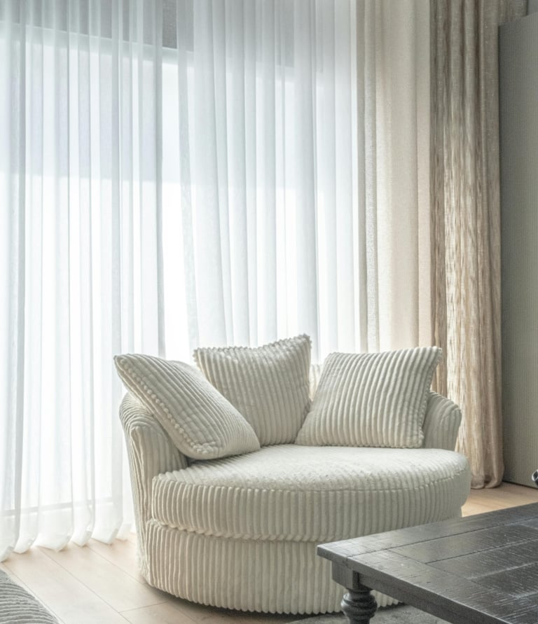 Soft linen curtains in neutral color framing a sunlit window with cozy chair beside