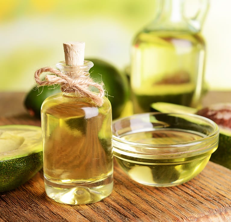 A glass bottle with a cork and twine, filled with a light golden liquid, avocado oil.