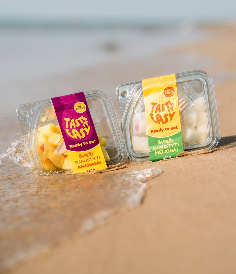 paplūdimyje ant smėlio padėti pjaustyto ananaso bei meliono indeliai