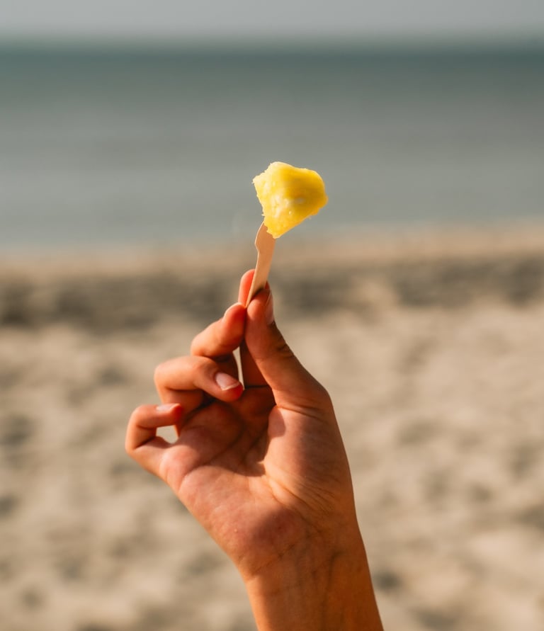 paplūdimio fone ant šakutės pasmeigtas pjaustyto ananaso gabaliukas