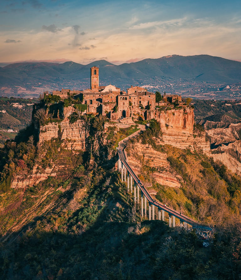 Panoramic view of the ancient hilltop village of Civita di Bagnoregio in Italy connected by a long pedestrian bridge.