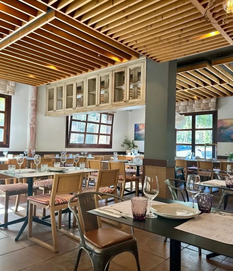 Interior del Restaurante con las mesas preparadas y un ambiente cálido de madera y luz natural.
