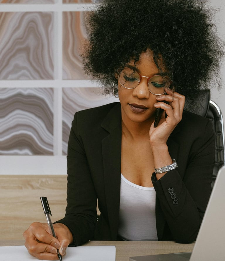 Une femme en tailleur noir au téléphone qui prend des notes sur une feuille