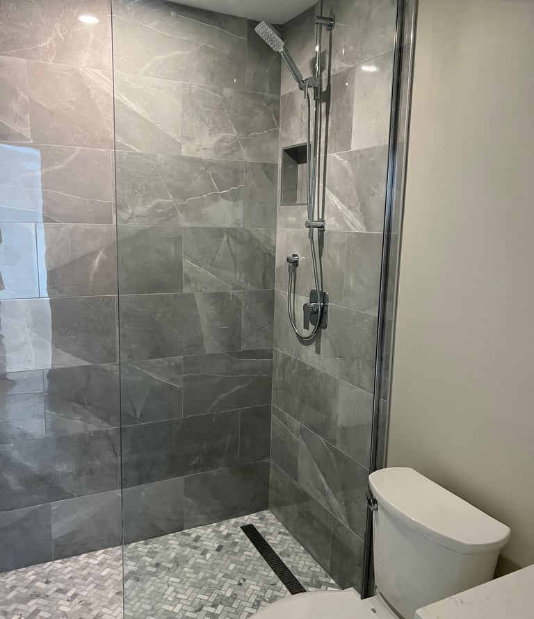 Modern walk-in shower featuring grey porcelain wall tiles, mosaic floor, and chrome fixtures.