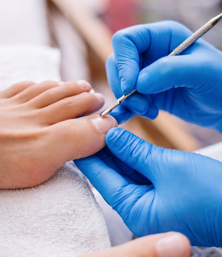 Professional nail technician in blue gloves performing a medical pedicure on a client's toenails