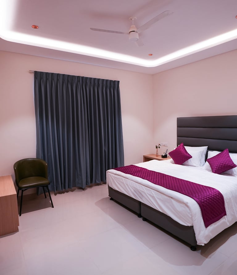 Modern hotel bedroom featuring a king bed with purple accents and ambient cove lighting.