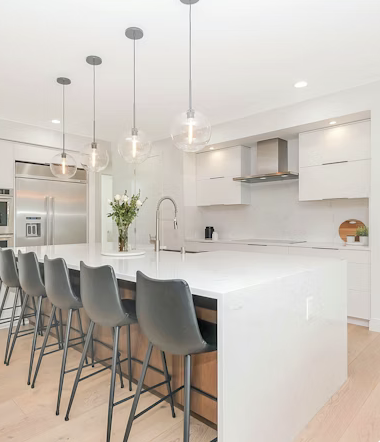 Open-plan kitchen renovation in Sussex featuring a white island with a breakfast bar, lighting, and integrated appliances.