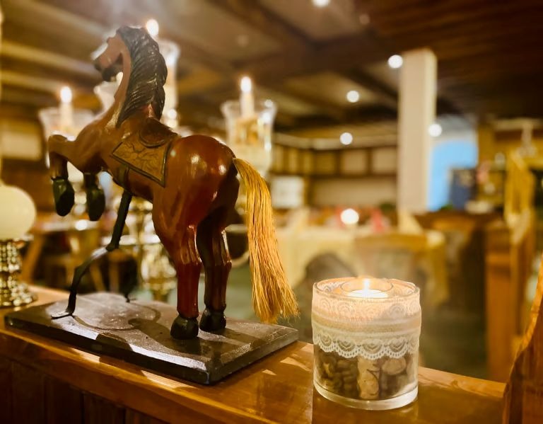 Wooden rearing horse statue next to a lit candle in a cozy, rustic restaurant setting.