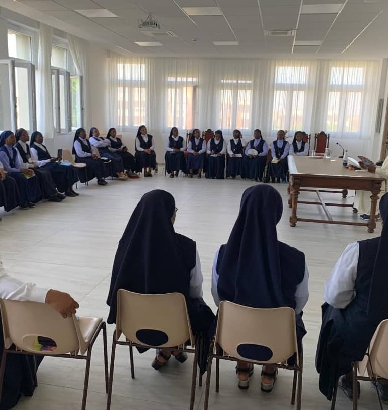 A large group of Catholic nuns in blue and white habits sitting in a circle for a meeting.