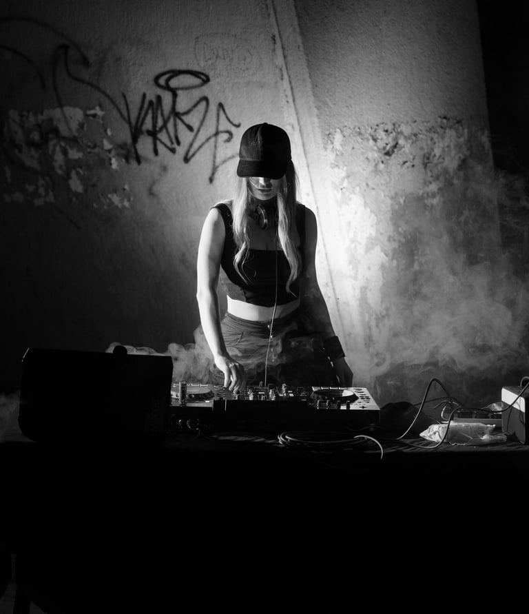 Kat Bendis wearing a cap mixes music on a pioneer rx3 in a smoky, underground club setting.