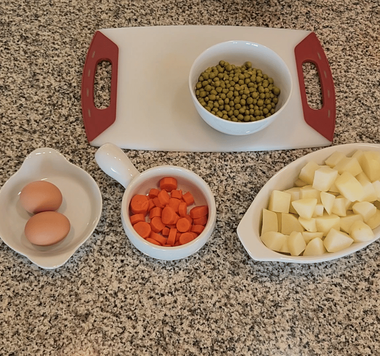 a cutting board on a counter with eggs, potatoes, carrots and peas