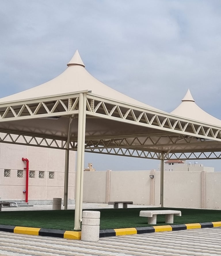 Two peak tent tensile structures providing outdoor shade over artificial turf and benches.