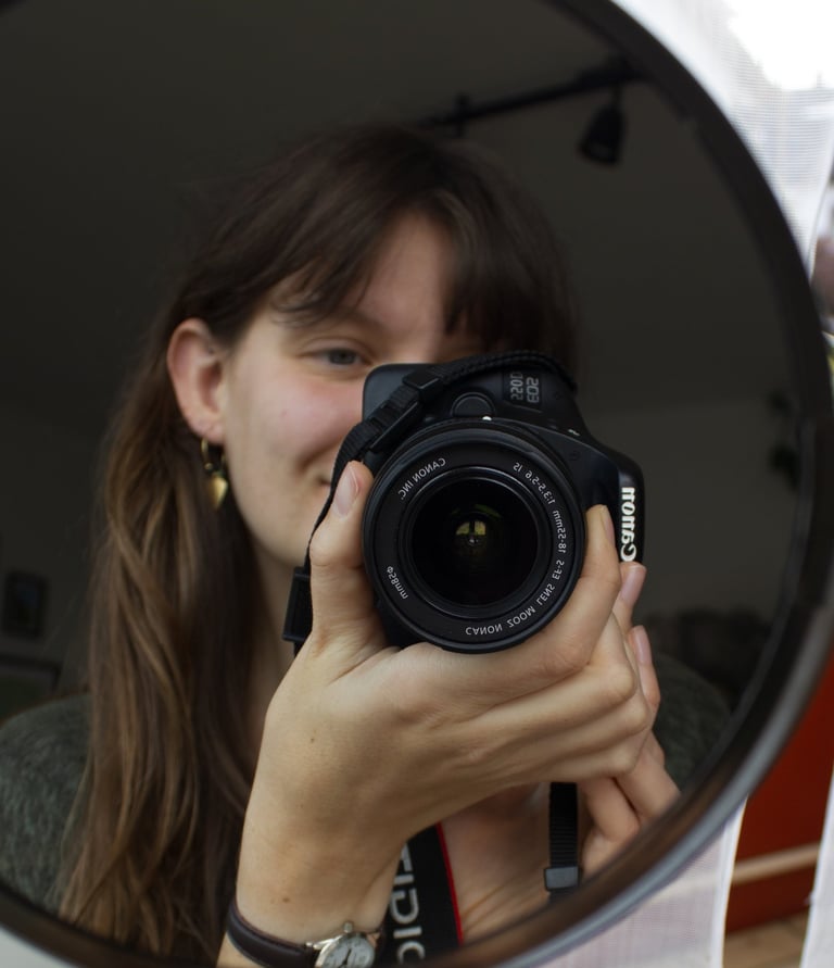 Caro hält eine Kamera und fotografiert sich im Spiegel. Ein persönlicher Einblick hinter die Kulisse