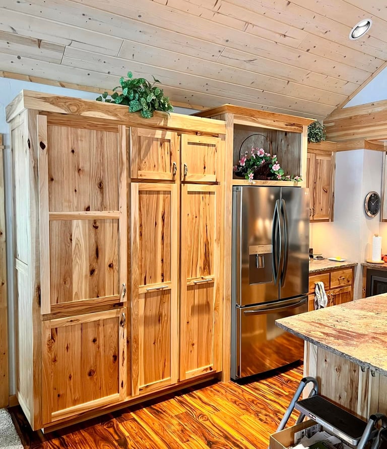 Rustic knotty pine kitchen cabinets with a stainless steel refrigerator and wood plank ceiling.