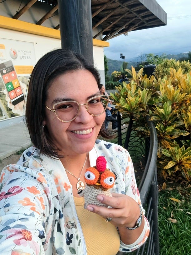 Una mujer sonriendo sosteniendo un amigurumi de gallineta