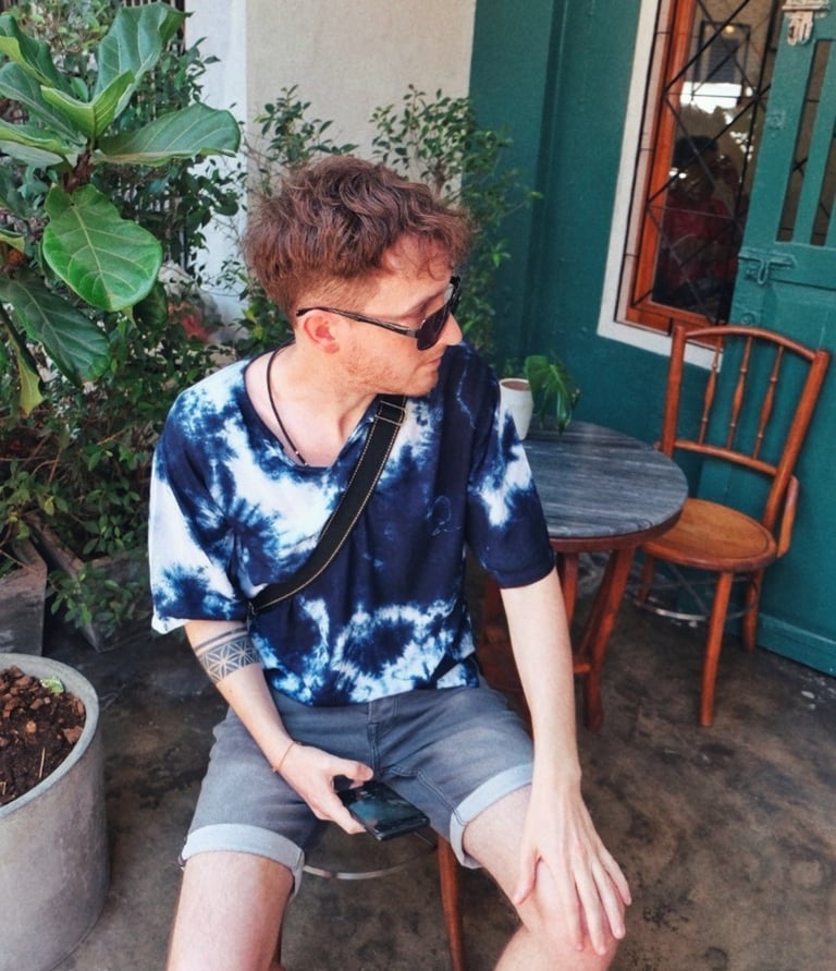 In a blue tie-dye shirt and sunglasses Unicris sitting at an outdoor cafe with plants.