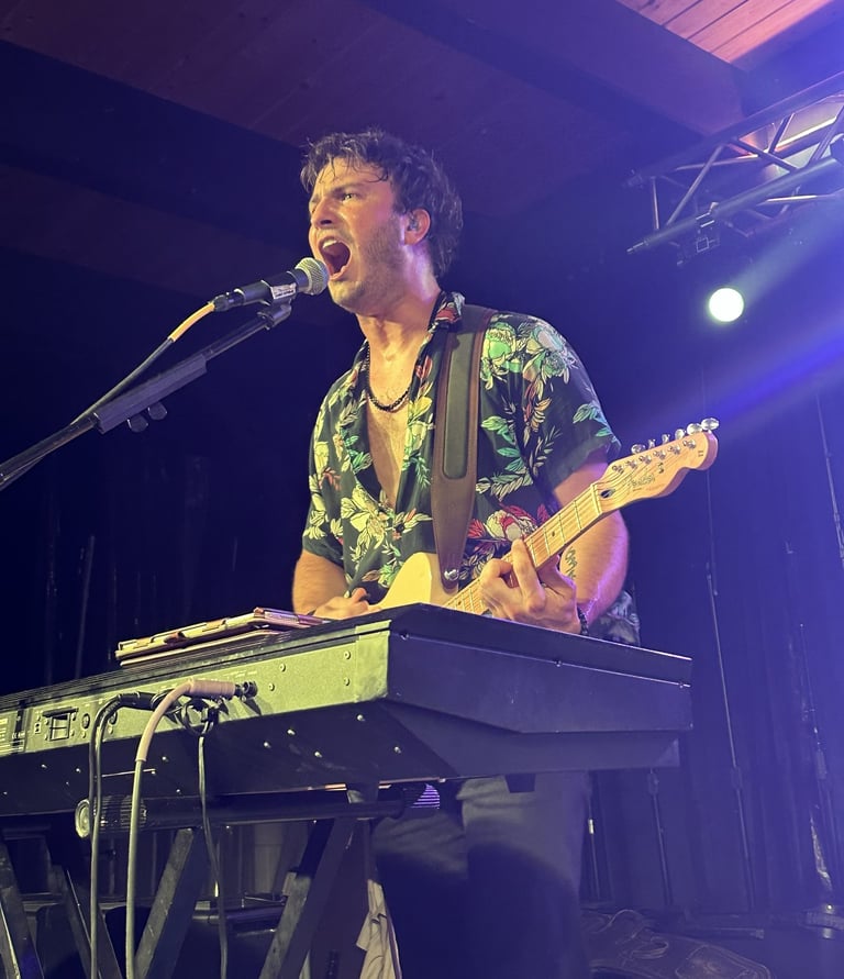 Male musician singing and playing electric guitar and keyboard during a live concert performance.
