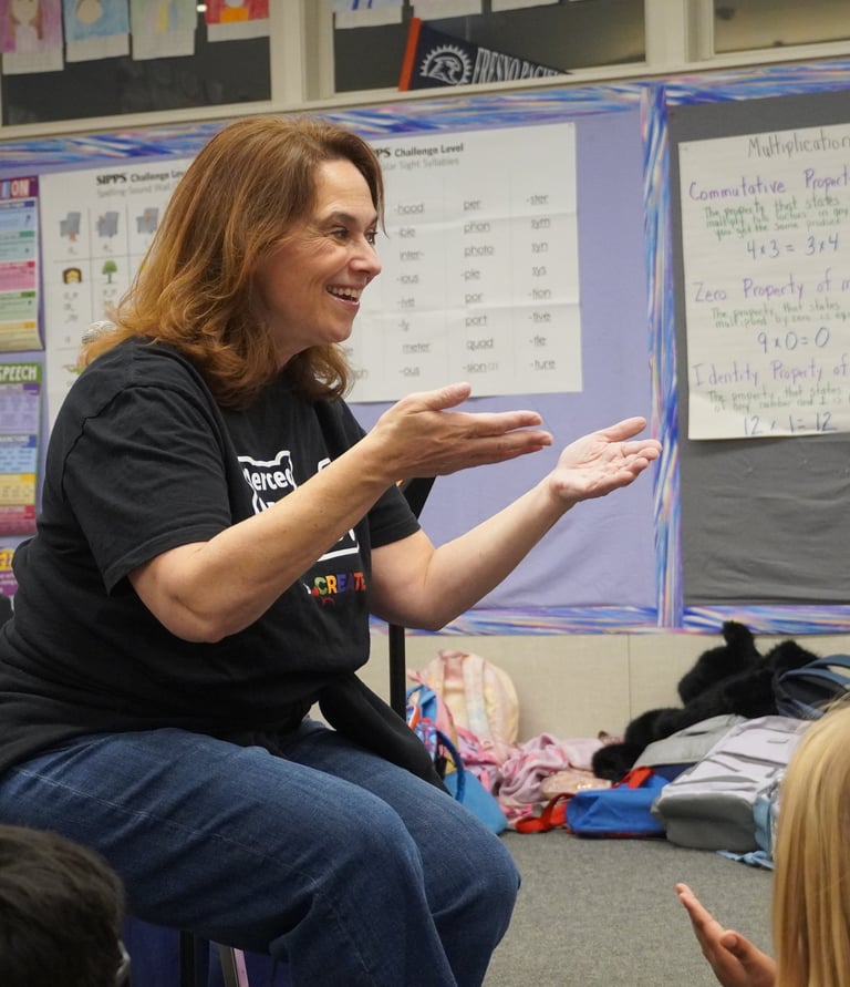 A smiling music teacher gestures while teaching a classroom lesson to students.