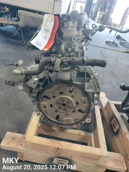 Used car engine assembly with flywheel on a wooden pallet in an auto parts warehouse.