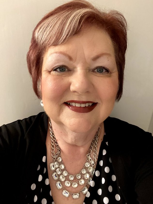 Photo of Debbie in front of a blank wall, wearing business black and jewelry.