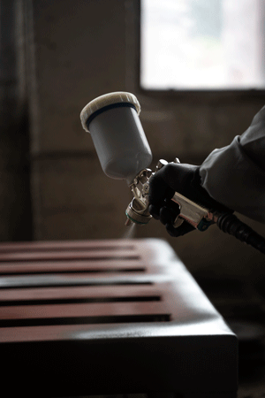 A gloved worker uses a professional spray gun to apply a fine paint finish to a metal surface.