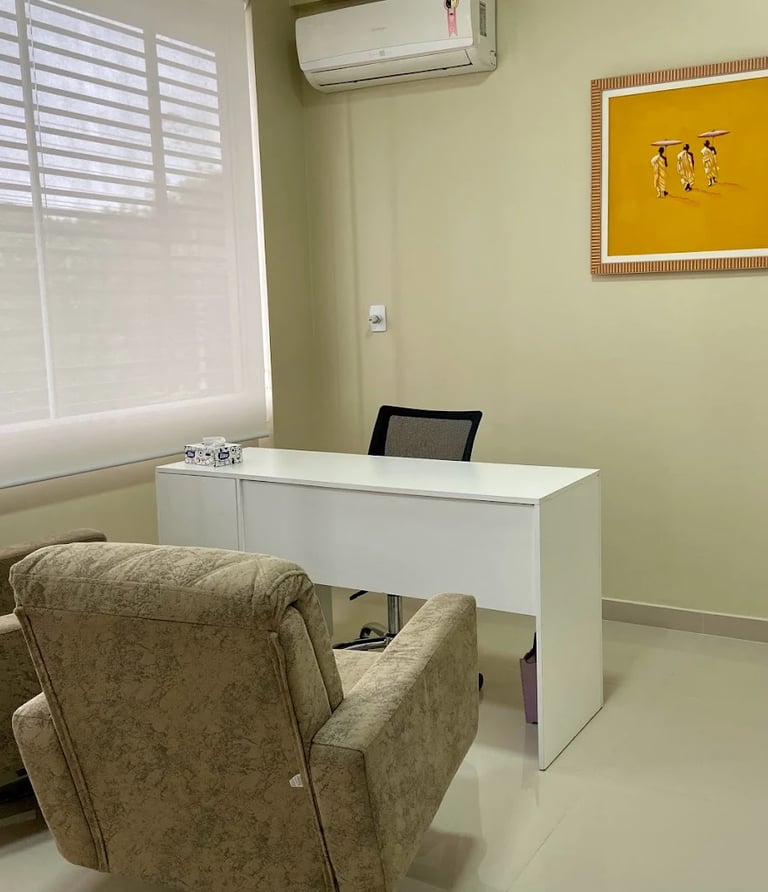 Um consultorio com uma mesa branca e duas poltronas.