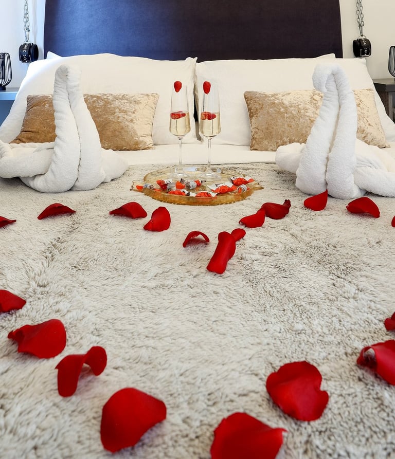 The photo shows a bed decorated for a honeymoon special in the BDSM Love Apartment with champagne and rose petals. 