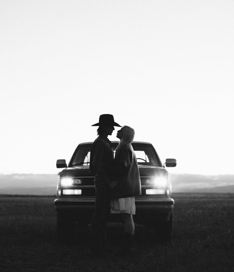 a man in a cowboy hat and a woman, facing each other in front of truck headlights