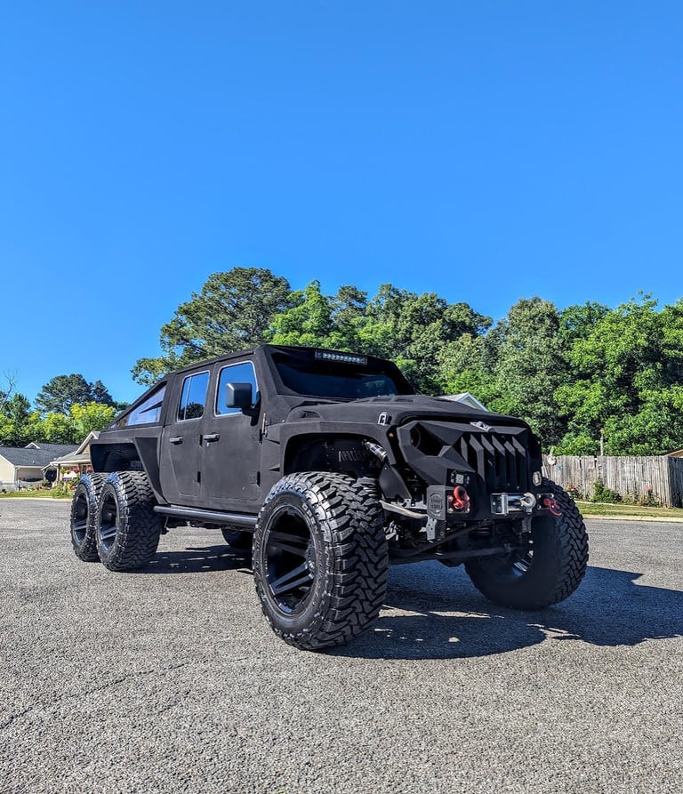 A matte black Apocalypse 6x6 truck with off-road tires parked on a sunny street.