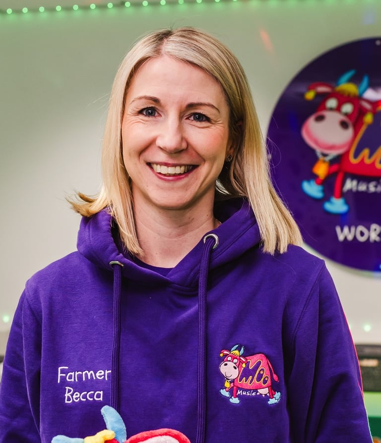 Farmer Becca stood in the Moo Room smiling, holding Maggie Moo in her branded purple Moo hoodie.