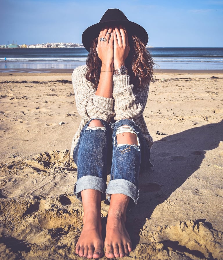 une femme qui se cache les yeux assise sur le sable