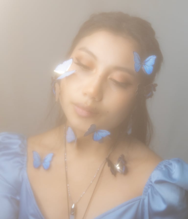 Same self portrait as home page, hazy dreamy with blue butterflies on face and neck.