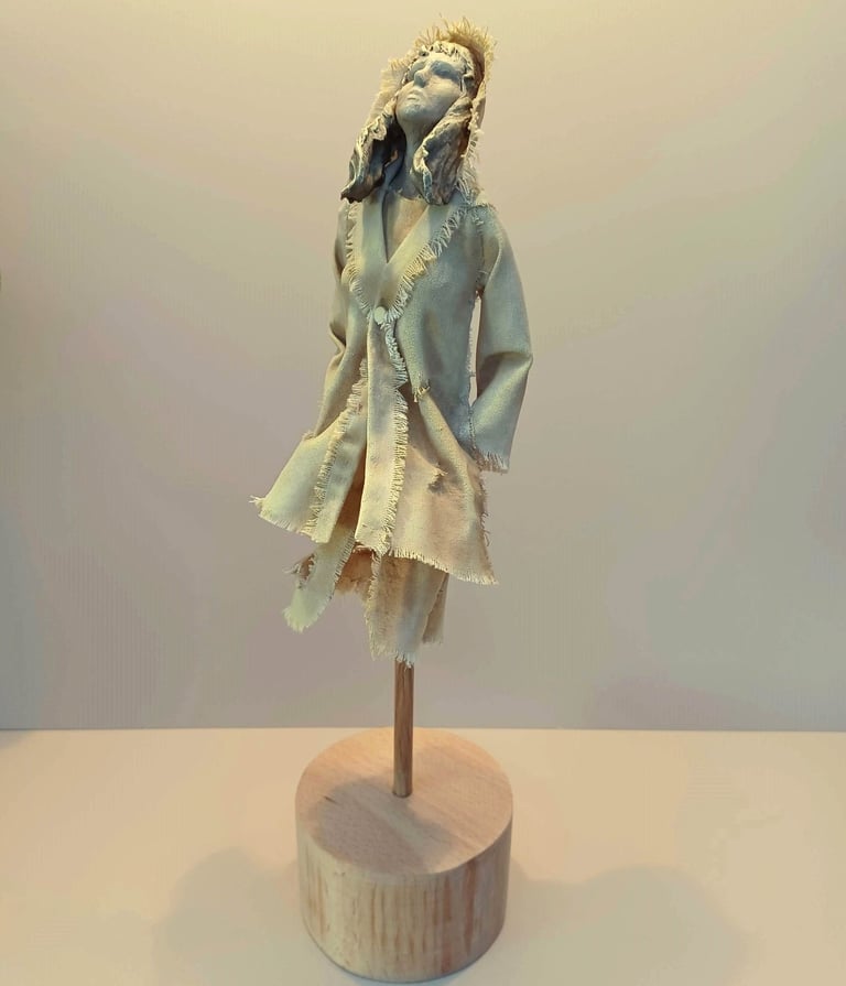 Clay and canvas sculpture of a female figure gazing upwards, wearing windswept, ragged clothes.
