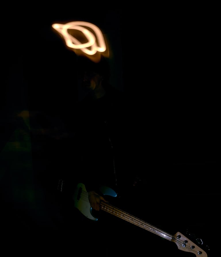 Musician playing a light blue bass guitar in the dark with orange light painting trails.