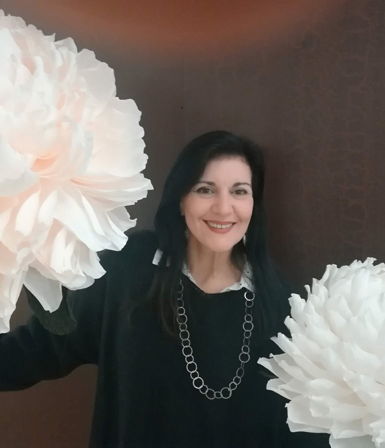 Clara Mennella sorride tra grandi fiori scenografici durante un evento legato al mondo del food & wine.