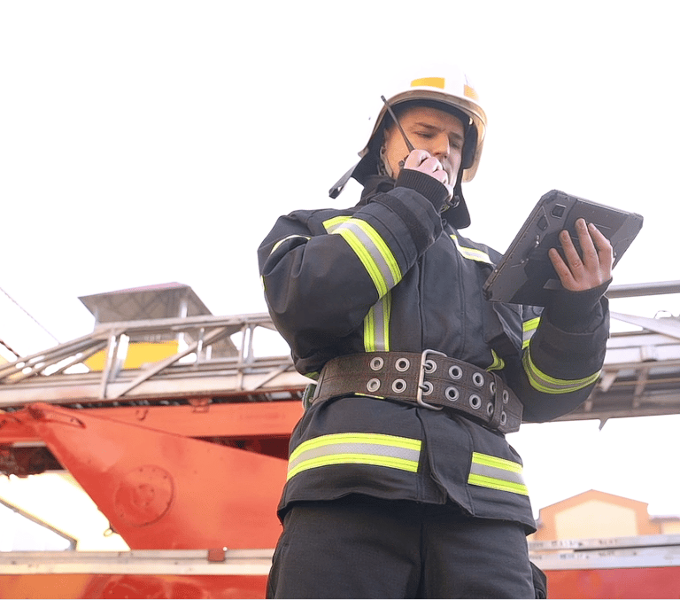 Firefighter speaking on a PoC radio and looking at information on a tablet