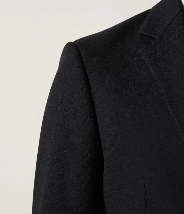 Close-up detail of a high-end black garment showing intricate stitching and premium texture. The lighting highlights the craftsmanship against an off-white #F8F8F8 background. Artistic and refined.