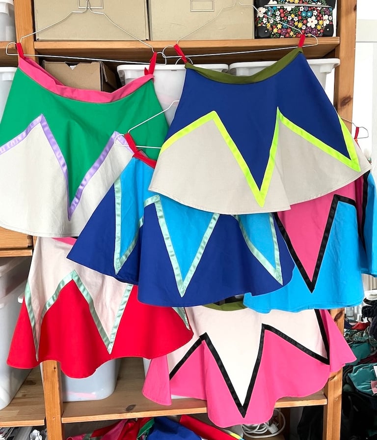 Handmade colorful circus skirts with zigzag patterns hanging on a wooden storage rack.