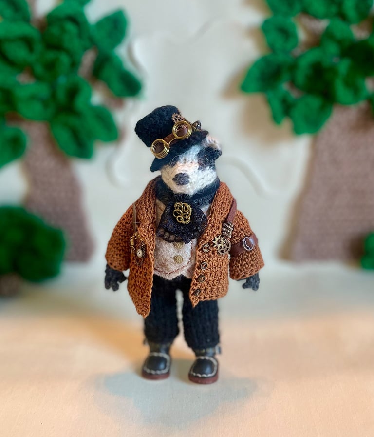 A handmade little knitted badger ornament wearing steampunk clothes 