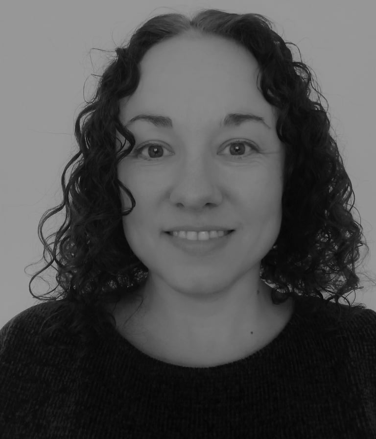 a woman with dark, curly hair and a black sweater. She is smiling.