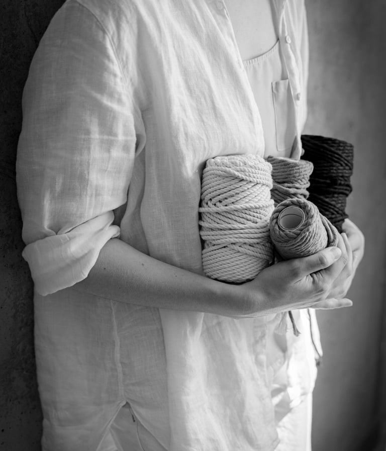 Black and white image of a person holding several spools of thick twisted rope, likely for macrame.