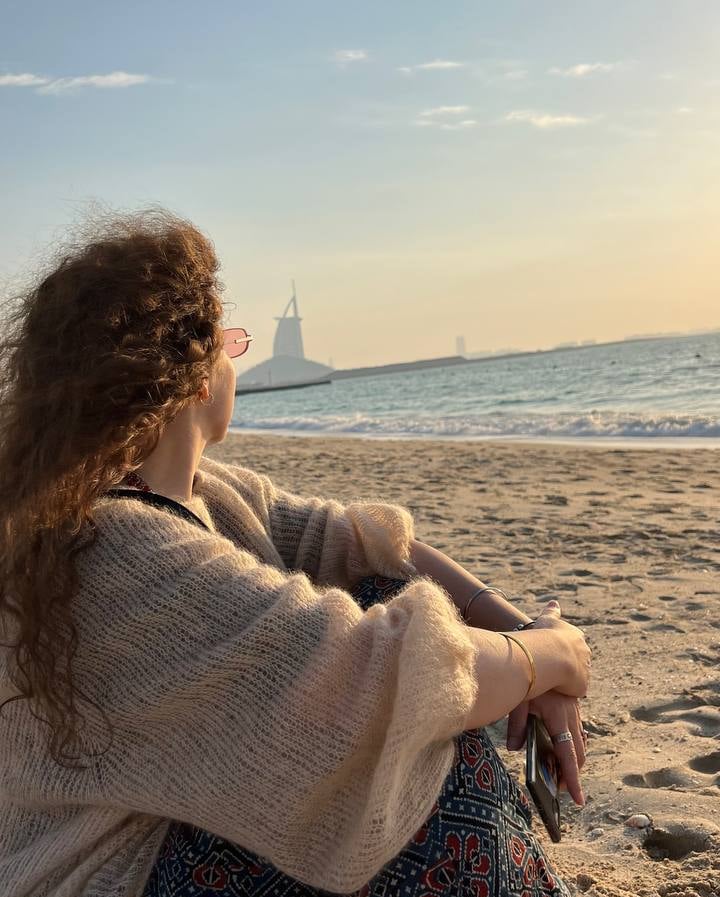 a woman sitting on a beach with a sailboat in the background