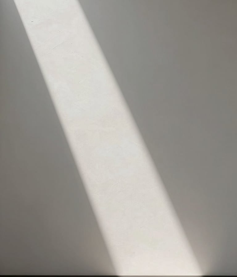 A vertical, high-end photography of a minimalist interior featuring a single beam of light crossing a textured white wall. The style is editorial and museum-like, focusing on the interplay of light and shadow. Palette of off-white and soft grays.