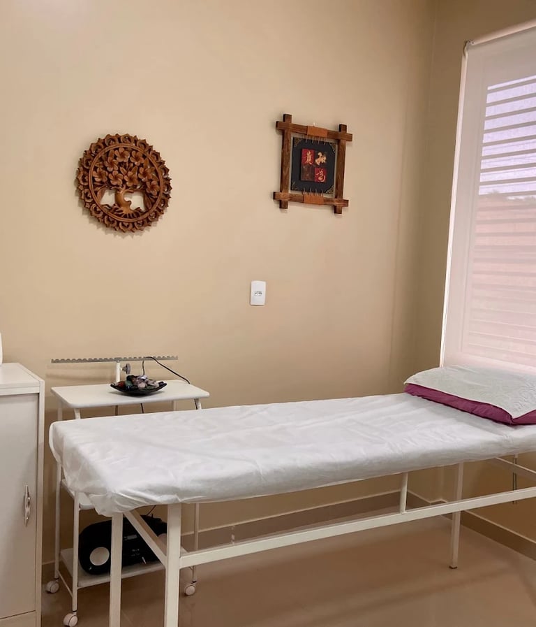 Um consultório com uma maca de terapia, alguns armários e quadros na parede.