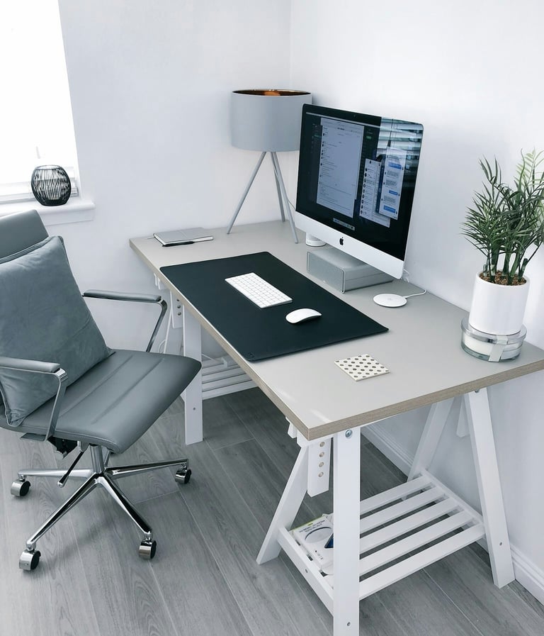 Modern home office setup with a gray ergonomic chair, white trestle desk, and an iMac computer.